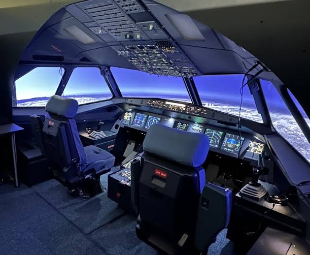 Airbus A320 fixed-base flight simulator cockpit with illuminated panels and runway visual display